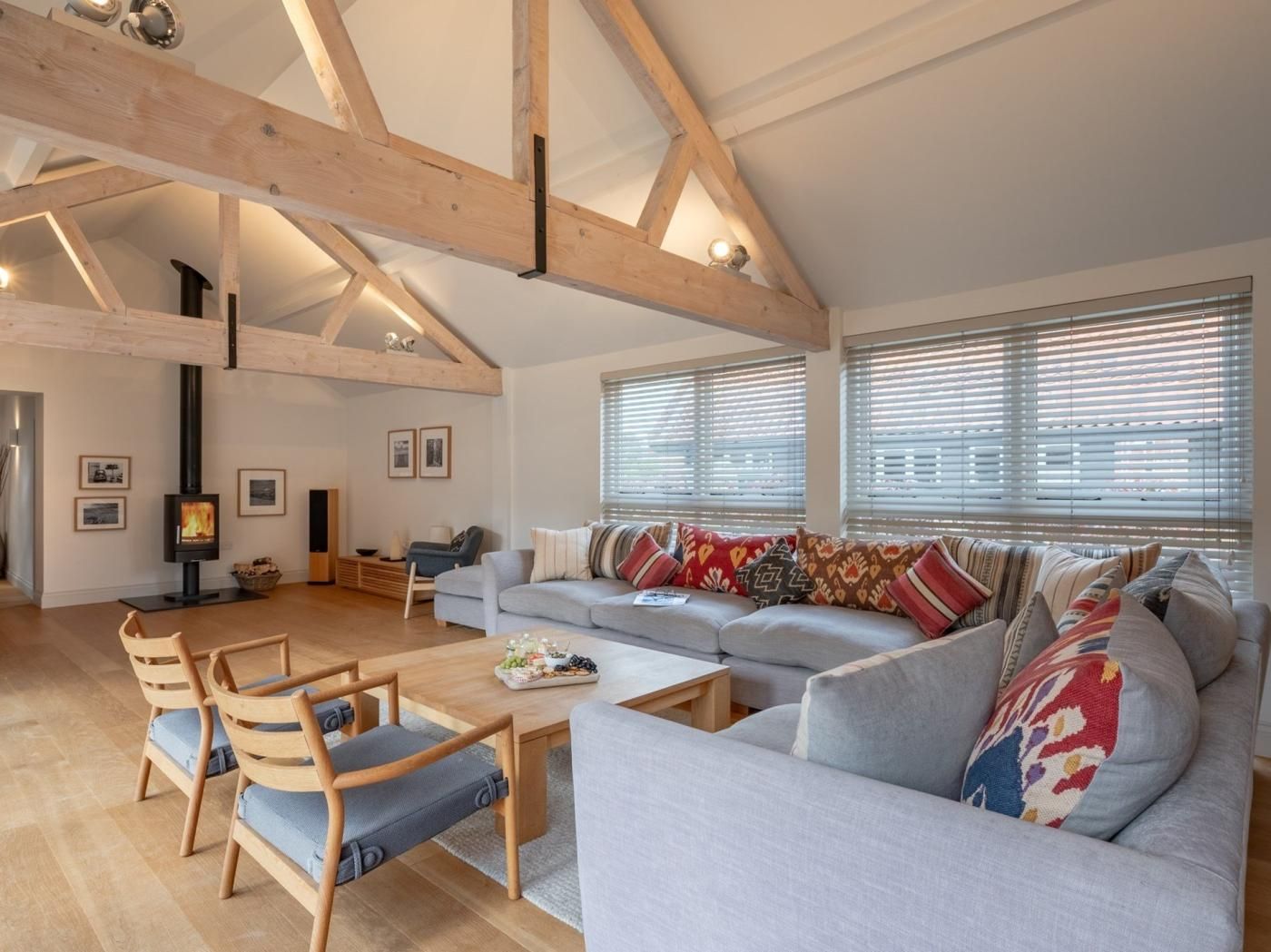 Een ruime woonkamer met een hoge plafond, houten balken, een open haard, een zithoek en een eettafel.