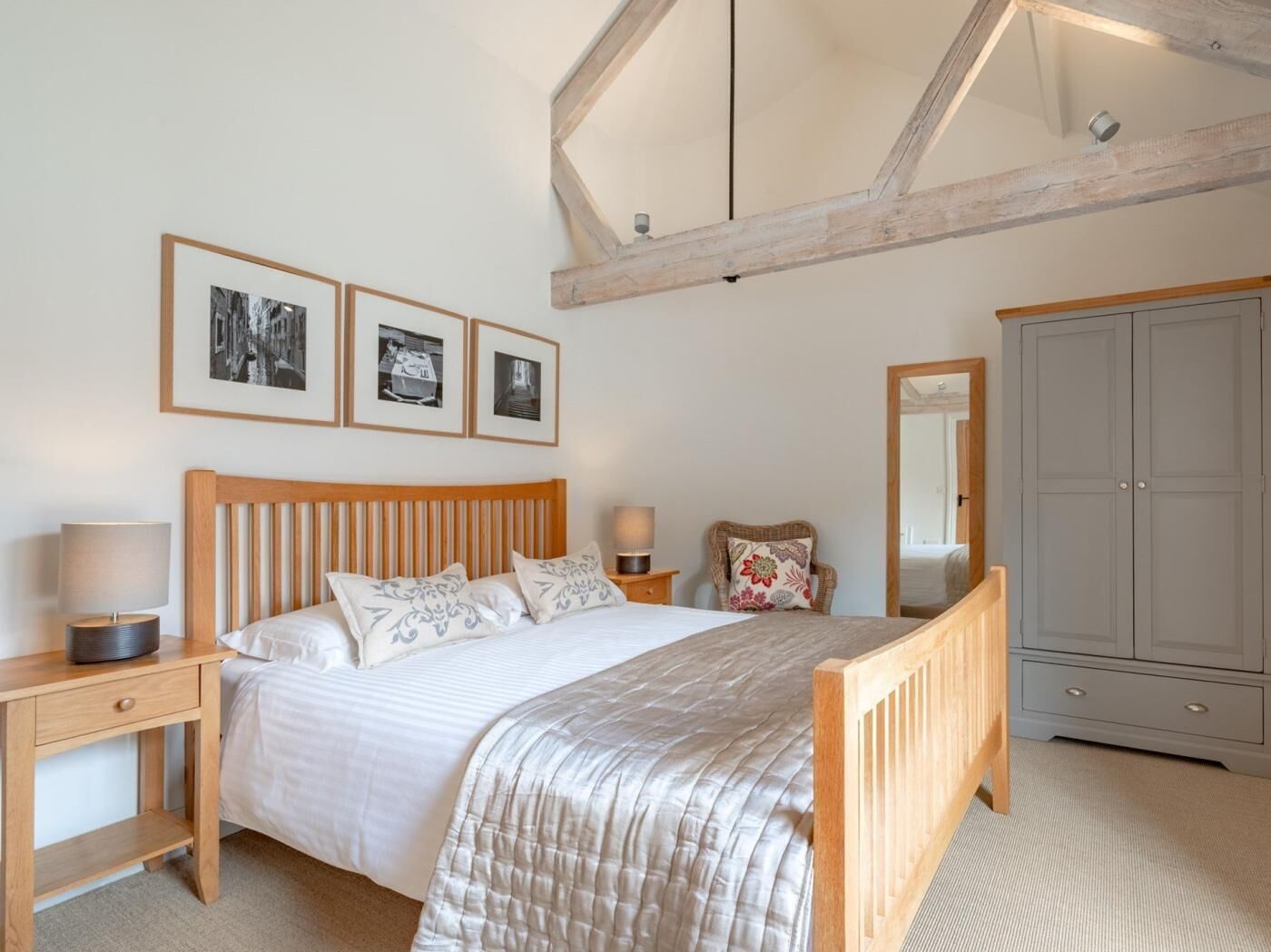 A bedroom with a wooden bed, bedside tables, a mirror, and framed pictures on the wall.