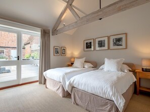 A bedroom with two beds, a large window, and a wooden ceiling beam. - 4 Bed in Worstead (oc-65189) (Worstead)