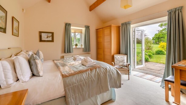 Een slaapkamer met een bed, een stoel, een kast en uitzicht op de tuin via een glazen deur.