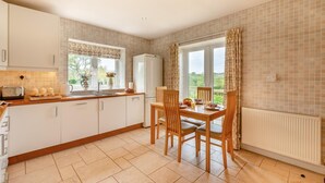 Een keuken met een eettafel, stoelen, een koelkast en een raam met gordijnen.