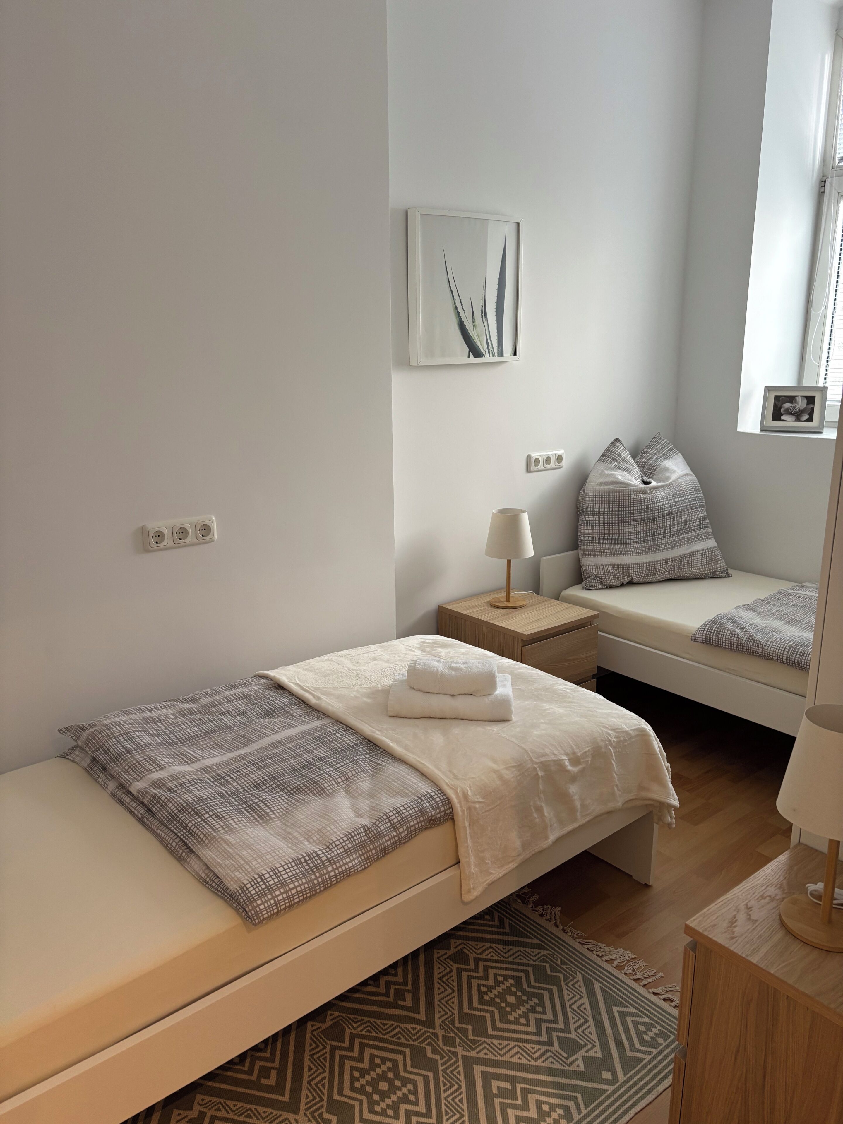 A minimalist bedroom with a single bed, bedside tables, a lamp, and a wall-mounted picture.