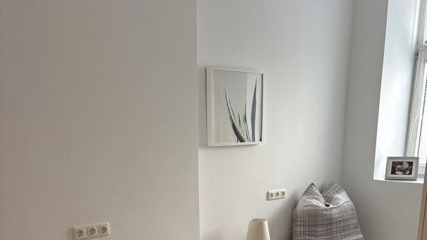 Una camera da letto minimalista con un letto singolo, comodini, una lampada e un quadro appeso al muro.