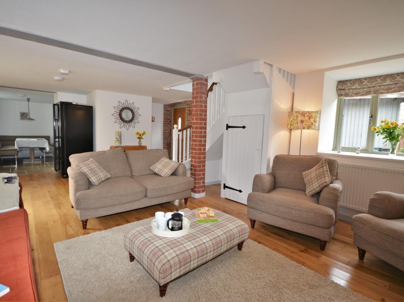 A living room with a sofa, ottoman, and a coffee table with cups and a book.