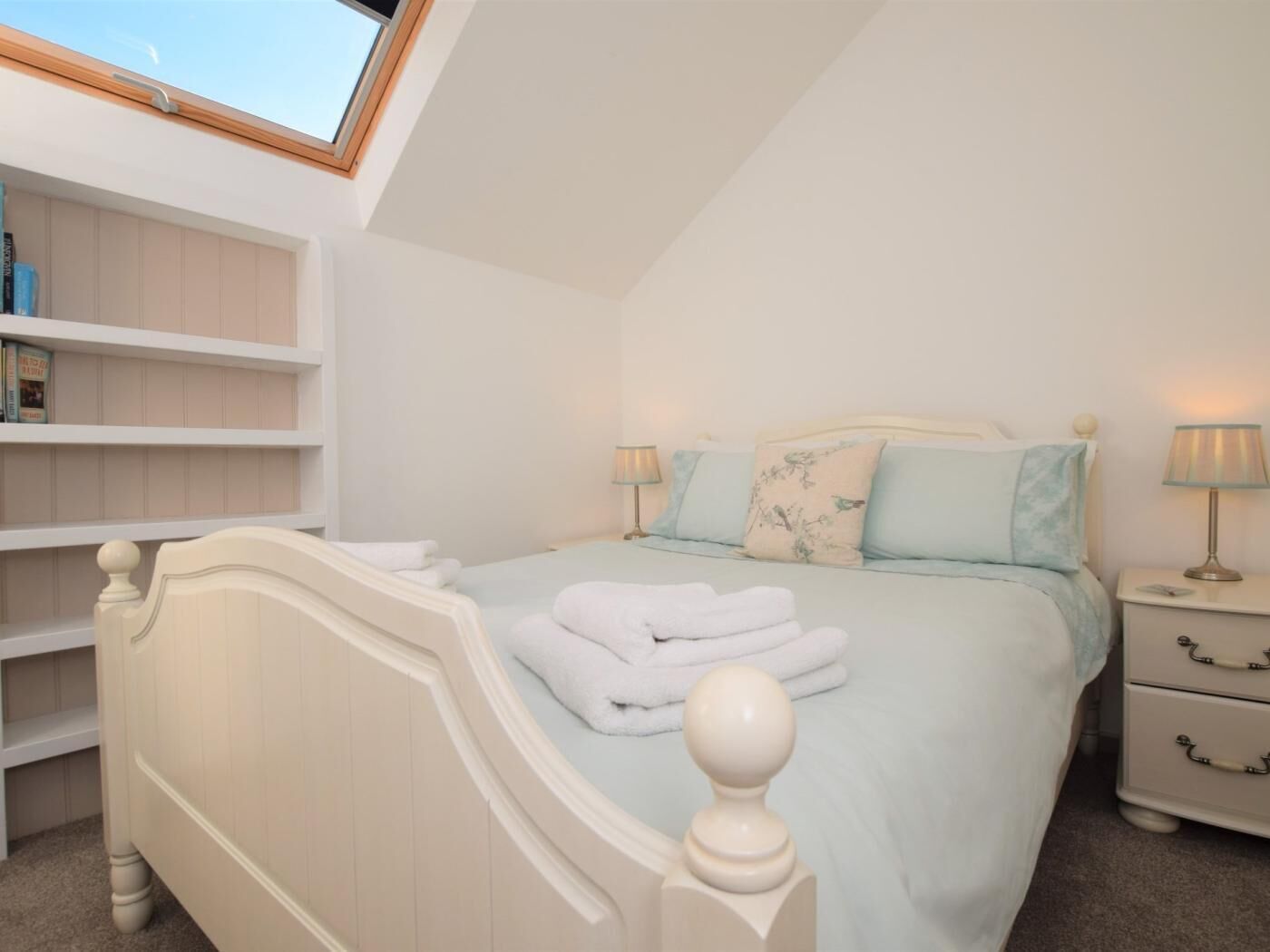 A bedroom with a bed, bedside tables, a nightstand, a shelf, and a skylight.
