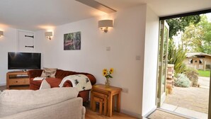 A modern living room with a sofa, TV, and a small table with a vase of flowers. - 3 Bed in North Tawton (oc-66043) (Bondleigh)