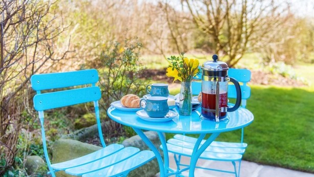A table with a coffee pot, cups, and a croissant, set outdoors with a blue chair and bench. - 3 Bed in Harrogate (oc-hh057) (Harrogate)