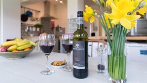 A bottle of Monte Givese wine, two wine glasses, a bowl of fruit, and a vase with yellow flowers on a table. - 3 Bed in Harrogate (oc-hh057) (Harrogate)