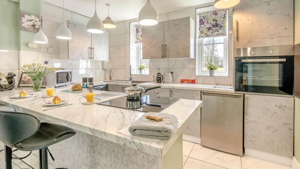 A modern kitchen with a marble countertop, stainless steel appliances, pendant lighting, and a large window. - 1 Bed in Beccles (oc-65080) (Beccles)