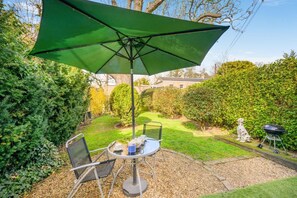Une terrasse avec une table et des chaises, un parasol vert et un barbecue.
