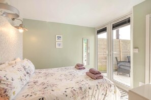 Une chambre à coucher comprenant un lit, un luminaire fixé au mur, une fenêtre et une porte donnant sur un espace extérieur.
