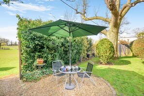 Une terrasse extérieure avec une table et des chaises, un parasol vert et une plante en pot.