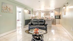 A modern living room with a glass coffee table, a black leather sofa, and a kitchen in the background. - 1 Bed in Beccles (oc-65080) (Beccles)