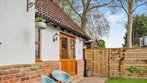 Een huis met een bakstenen gevel, een houten deur en een kleine tuin met twee stoelen en een grindpad.