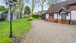 Een grindpad leidt naar een traditionele cottage met pannendak, een houten deur en een bordje met de tekst 'The Lodge'.