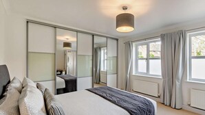 Een slaapkamer met een bed, een spiegel, een raam met gordijnen en een plafondlamp.