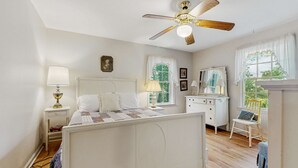 Un dormitorio con cama, ventilador de techo, cómoda, silla y ventana con cortinas.