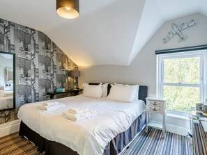 Quarto de hotel com cama, mesa de cabeceira, luminária, janela com vista e decoração de avião na parede.