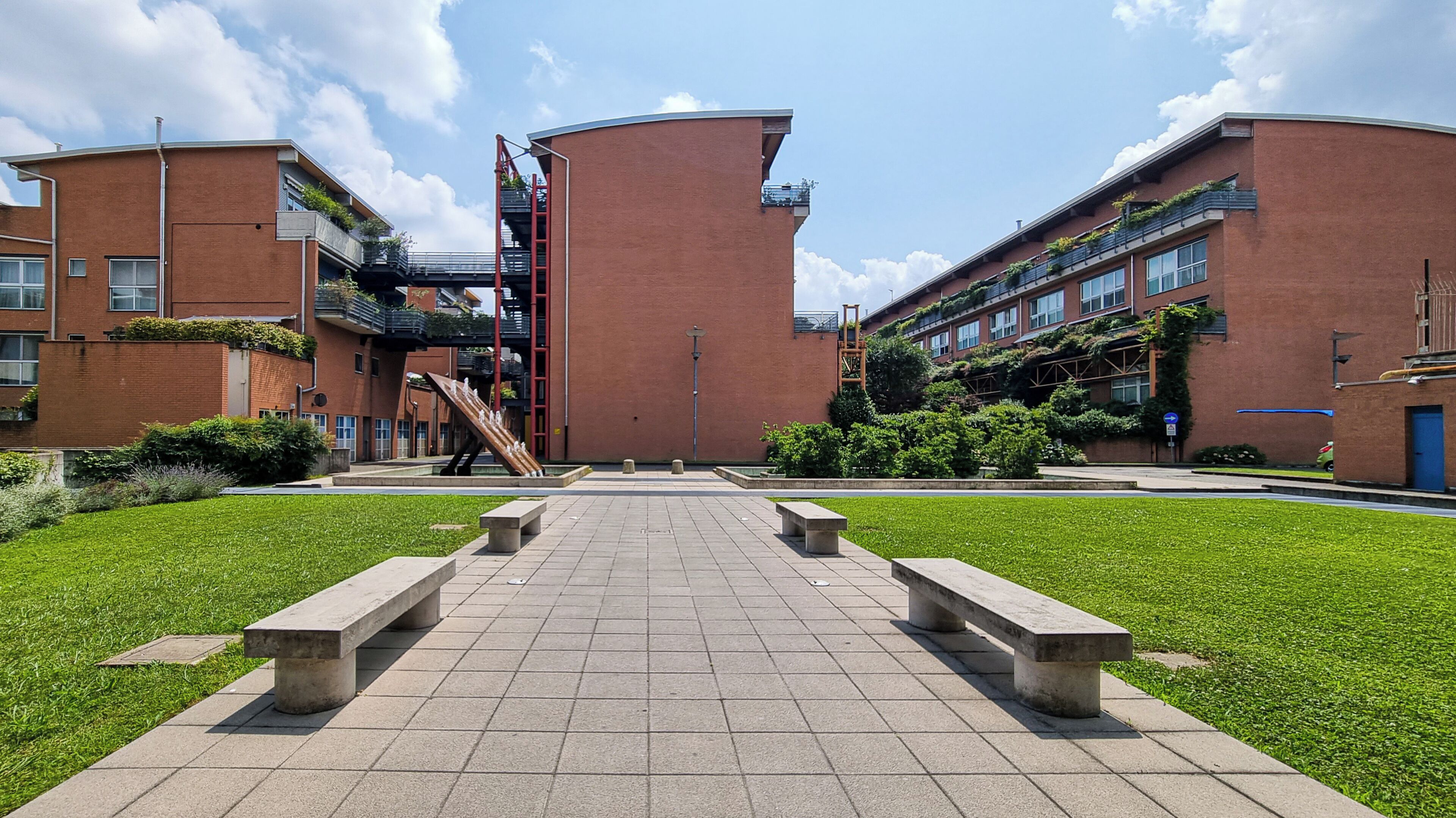 Een modern gebouw met een centrale trap, omgeven door een verhard gebied met banken.