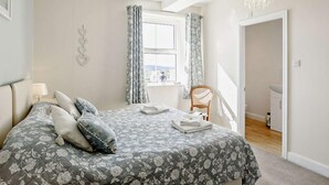 A bedroom with a bed, a chair, a window with curtains, a chandelier, and a view of a bathroom. - 2 Bed in Harrogate (oc-hh018) (Lindley)