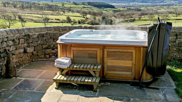 A hot tub with a stone wall backdrop, a wooden bench, and a towel stack. - 2 Bed in Harrogate (oc-hh018) (Lindley)