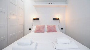 Et hotelværelse med en seng, to sengeborde med lamper, en dør og en lille hylde med pynteting.