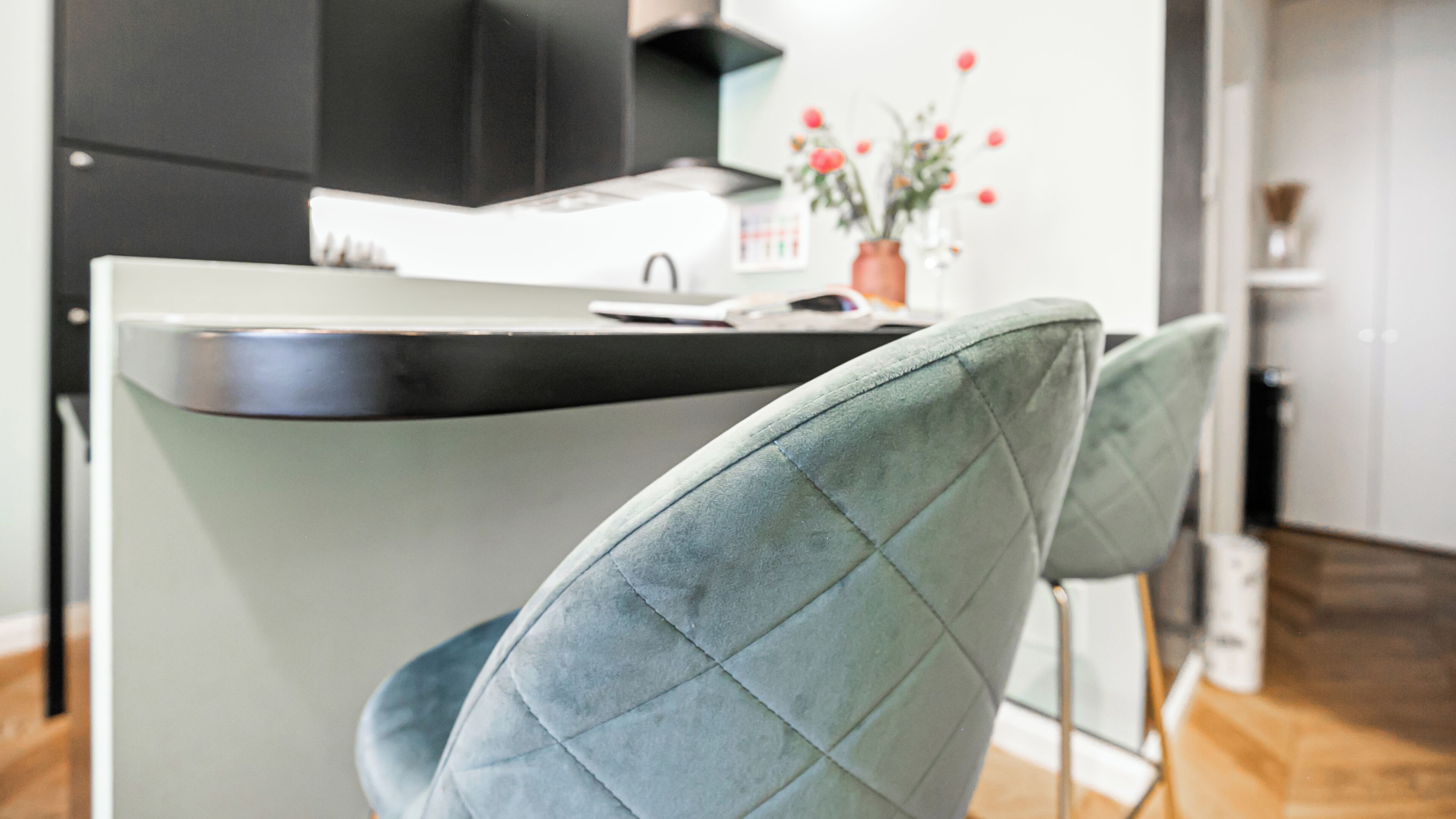 A modern kitchen with a central island, two upholstered chairs, a vase with flowers, and a calendar on the wall.