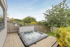 A hot tub on a wooden deck with a wooden fence and greenery in the background. - 3 Bed in Newton Abbot (oc-64380) (Bovey Tracey)