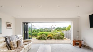 Ein modernes Wohnzimmer mit einer Couch, einem Couchtisch und Blick auf einen Garten durch eine Glastür.