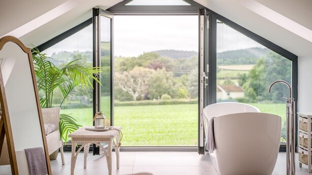 Ein modernes Zimmer mit Dachfenster, einer Badewanne, einem Tisch mit einer Laterne und Blick auf eine grüne Landschaft.
