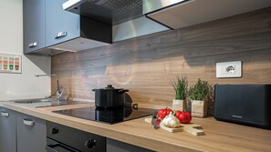A modern kitchen with a black induction cooktop, wooden countertop, stainless steel cabinets, and a built-in range hood. - Italianway Comfort - Da Messina 20 (Milano)