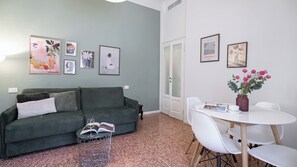 Ein Wohnzimmer mit einem grünen Sofa, einem runden Couchtisch und einem Essbereich mit einem weißen Tisch und Stühlen.