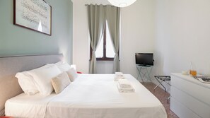 A hotel room with a bed, a TV, a desk with a chair, and a window with curtains. - Italianway Comfort - Da Messina 20 (Milano)