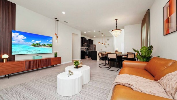 A modern living room with a flat-screen TV, a leather sofa, a dining area, and a kitchen in the background. - 6BR at Windsor Cay - Private Pool, Spa & Themed Rooms (Clermont)