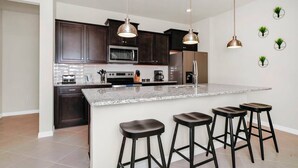 A modern kitchen with dark wood cabinets, stainless steel appliances, a granite countertop, and three bar stools. - 6BR at Windsor Cay - Private Pool, Spa & Themed Rooms (Clermont)