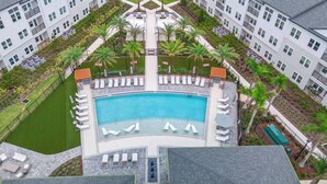 A rooftop pool with sun loungers, surrounded by greenery and a building with multiple balconies. - 6BR at Windsor Cay - Private Pool, Spa & Themed Rooms (Clermont)