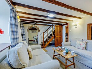 A cozy living room with a sofa, a wooden coffee table, and a staircase leading to a dining area. - 4 Bed in Brancaster (oc-kt196) (Brancaster)