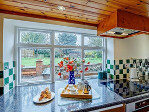 A kitchen with a large window, a tray with croissants, a coffee maker, and a vase with flowers. - 4 Bed in Brancaster (oc-kt196) (Brancaster)