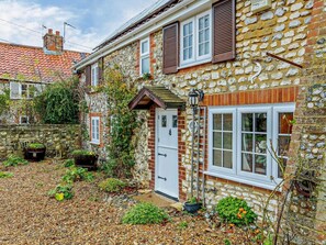 A stone house with a gravel driveway, a wooden door, and a small garden with plants and a statue. - 4 Bed in Brancaster (oc-kt196) (Brancaster)
