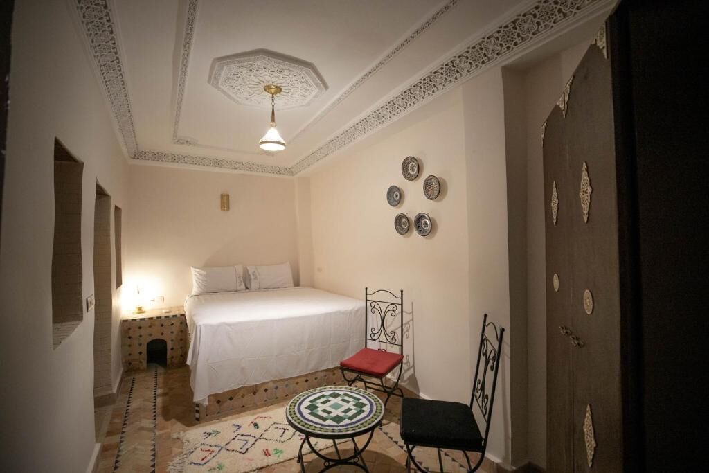 A bedroom with a bed, a chair, a small table, decorative plates on the wall, and a patterned rug.