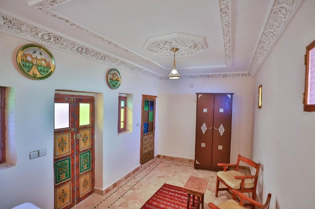 A room with ornate ceiling, a wooden door with glass panels, a red patterned rug, and a wooden chair.