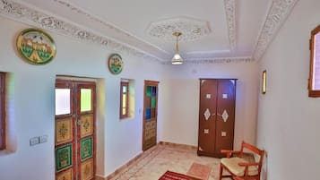 A room with ornate ceiling, a wooden door with glass panels, a red patterned rug, and a wooden chair.