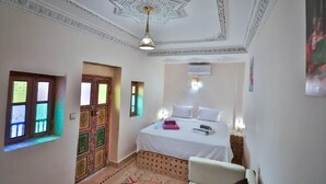 A bedroom with a bed, a chair, a patterned door, and a decorative ceiling.