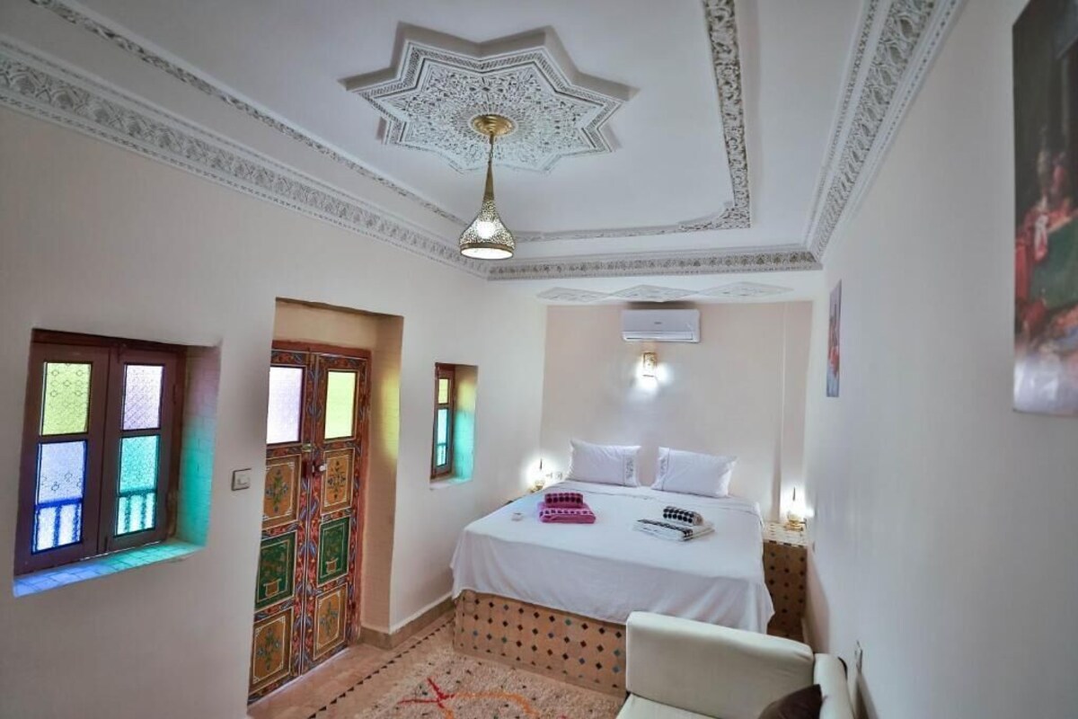 A bedroom with a bed, a chair, a patterned door, and a decorative ceiling.