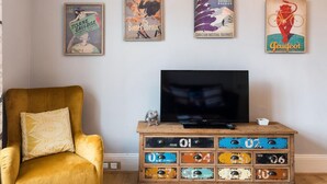 Ein Wohnzimmer mit einem gelben Sessel, einem Fernseher und Wandbildern im Vintage-Stil.