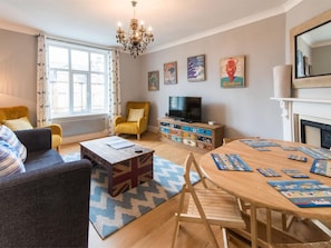Un salon comprenant un canapé, un fauteuil, une table basse en bois et une table à manger avec des sets de table.