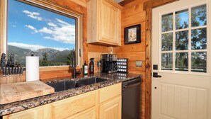A kitchen with wooden cabinets, granite countertops, a coffee maker, and a view of mountains.