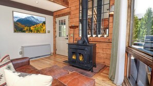 A cozy room with a fireplace, leather furniture, a large window, and a mountain view painting.