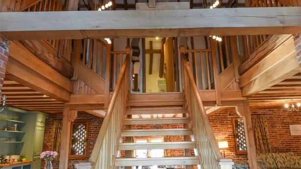Eine Holztreppe führt zu einer Schlafgalerie mit freiliegenden Balken und Backsteinwänden.