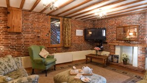 Ein gemütliches Wohnzimmer mit Backsteinwand, Fernseher, Kamin und gemusterten Möbeln.